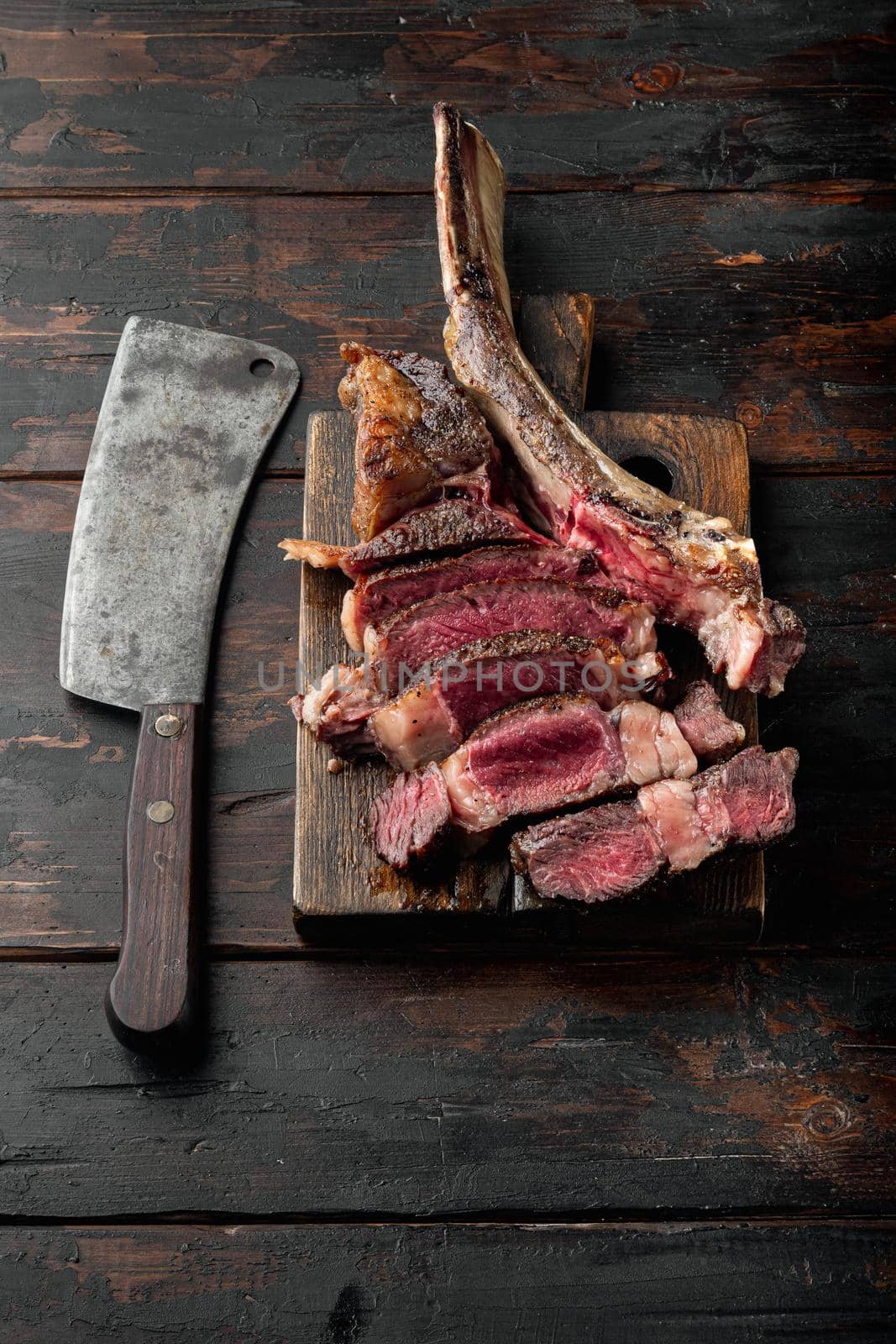 Sliced medium rare grilled Beef steak set, tomahawk cut, on wooden serving board, on old dark wooden table background, with copy space for text