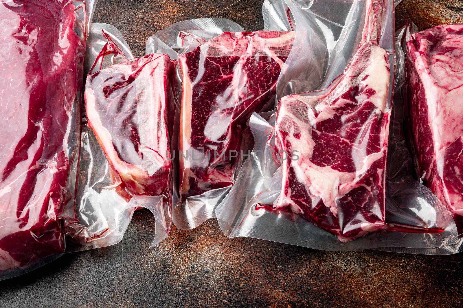 Vacuum packed organic raw beef classic cuts, tomahawk, t bone, club steak, rib eye and tenderloin cuts, on old dark rustic background by Ilianesolenyi