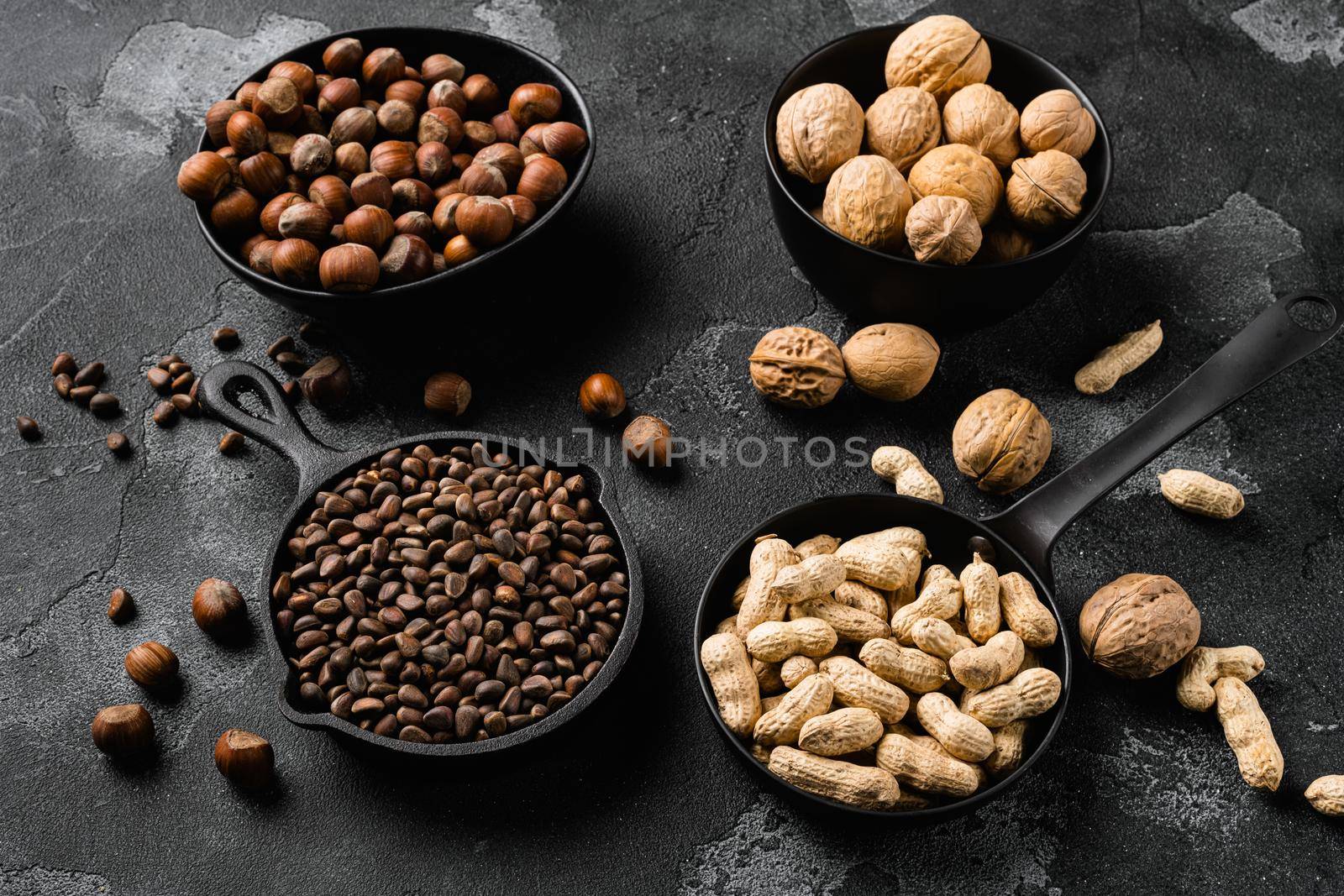 Assortment of nuts in shells, peanut, walnut, pine nuts and hazelnut, on black dark stone table background by Ilianesolenyi