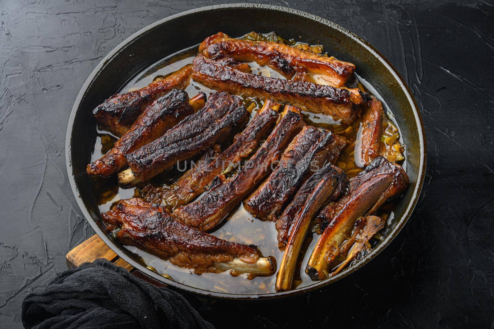 Grilled pork rib, in frying cast iron pan, on black stone background by Ilianesolenyi