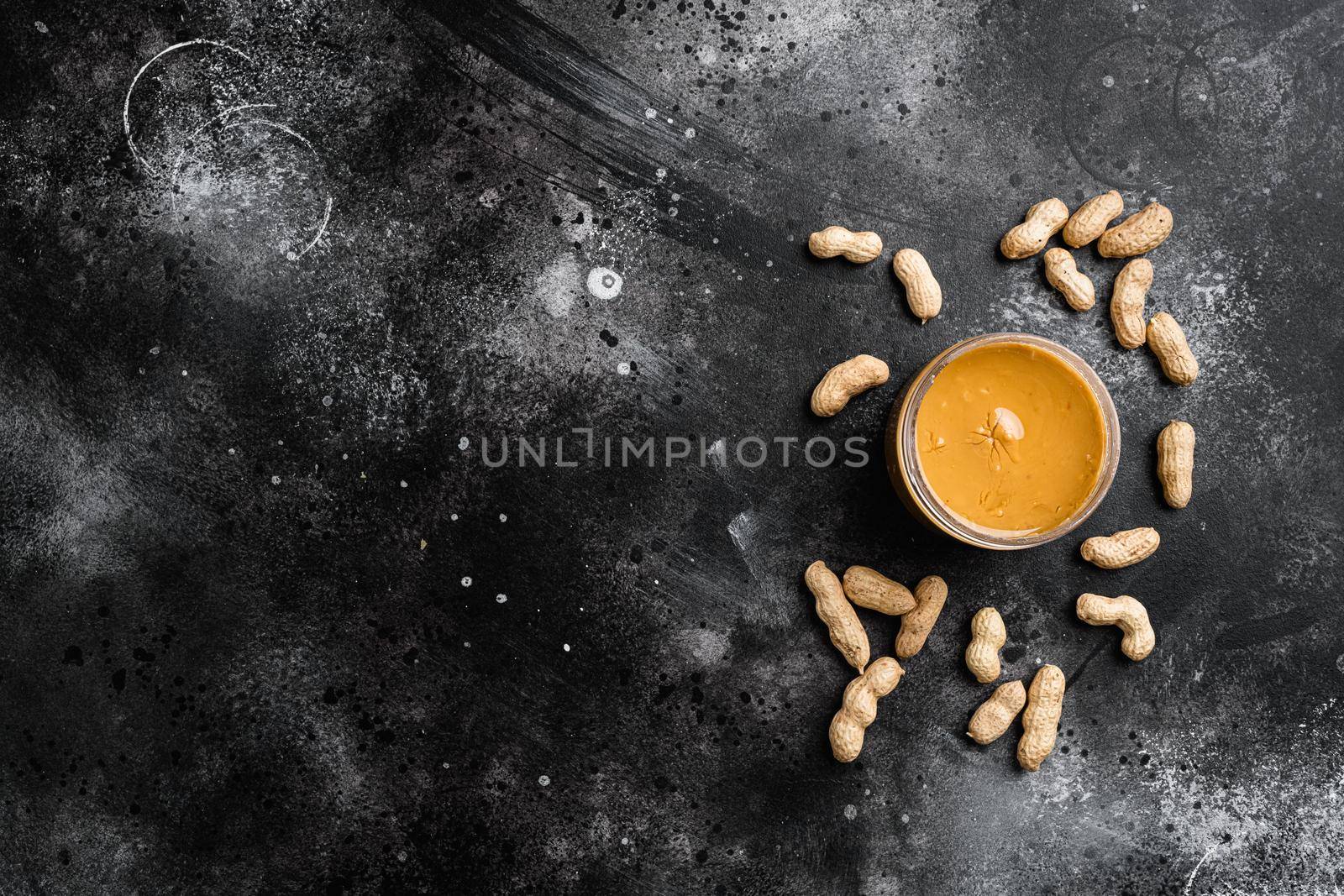 Peanut paste in an open jar and peanuts, on black dark stone table background, top view flat lay, with copy space for text by Ilianesolenyi