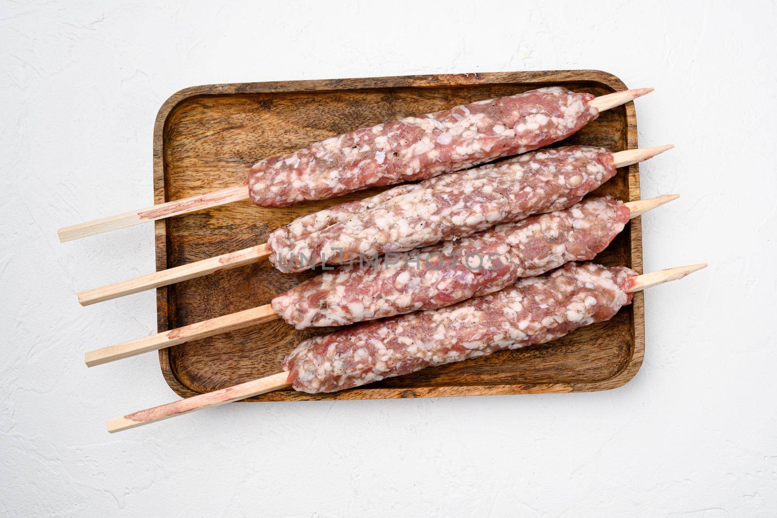 Uncooked Raw beef and lamb meat kebabs sausages, on white stone table background, top view flat lay by Ilianesolenyi