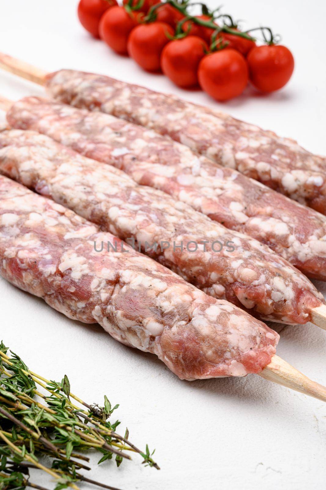 Minced and shaped lamb mutton kebabs, with grill ingredients, on white stone table background by Ilianesolenyi