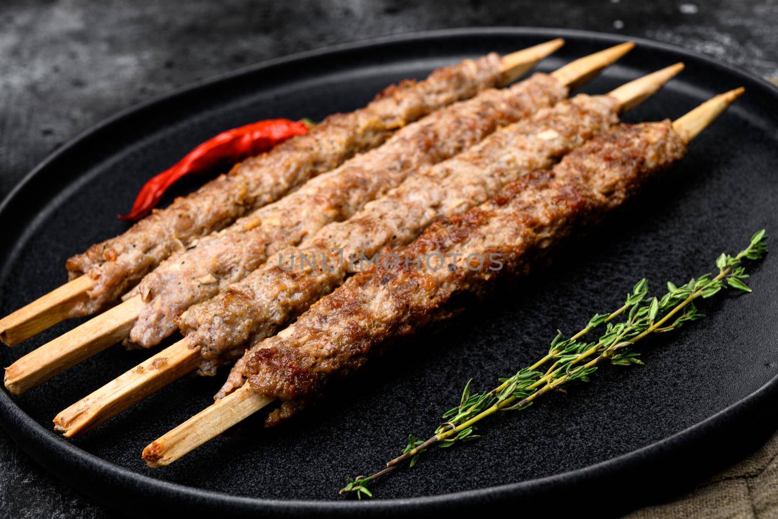 Minced and shaped lamb mutton kebabs set, on plate, on black dark stone table background