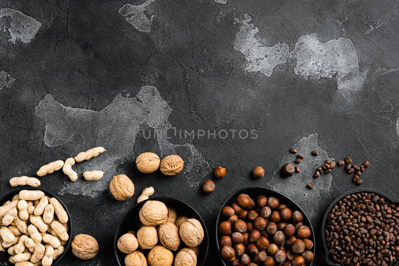 A variety of nuts, peanut, walnut, pine nuts and hazelnut set, on black dark stone table background, top view flat lay, with copy space for text