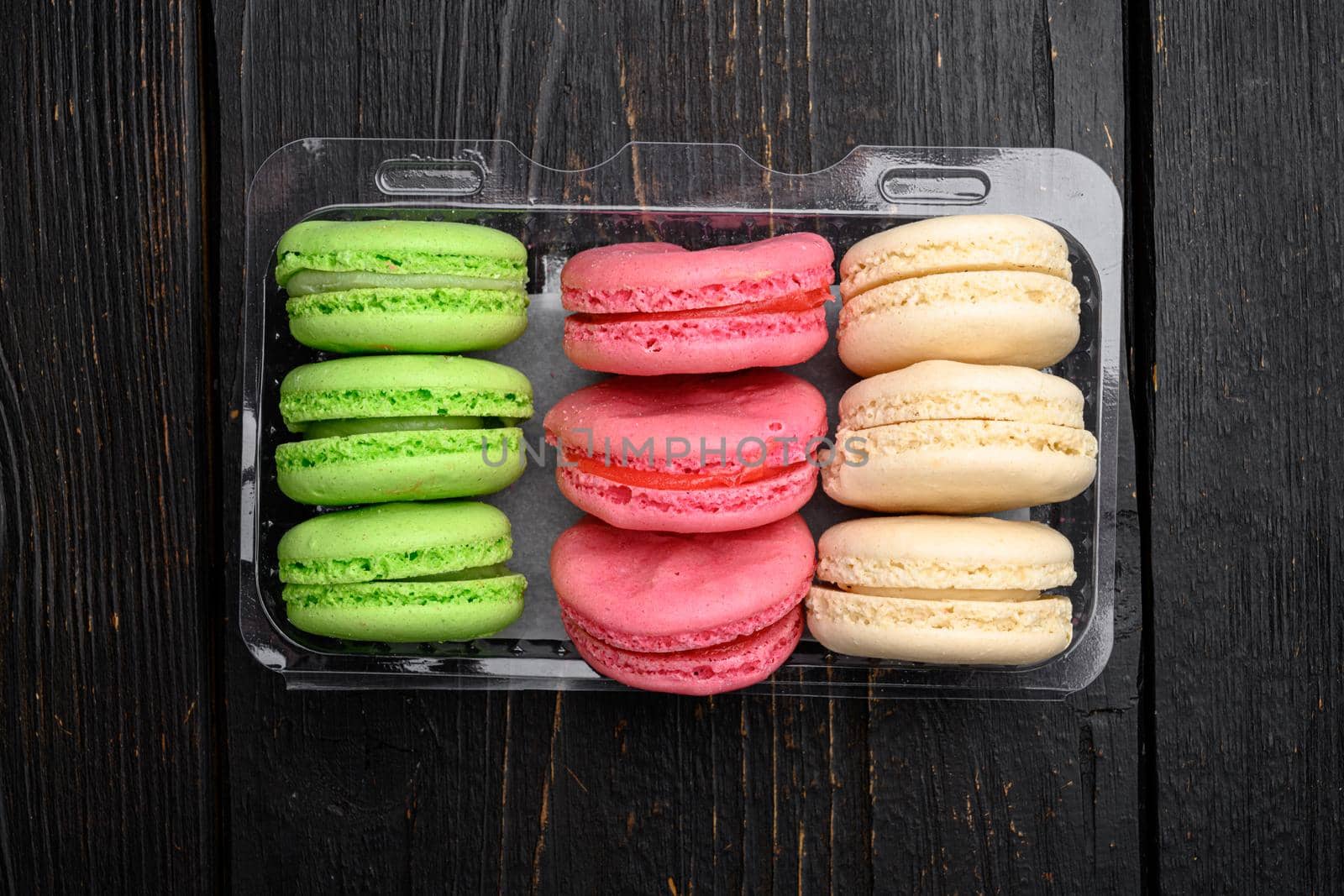 Dessert cake macaron or macaroon set, in plastic pack, on black wooden table background, top view flat lay
