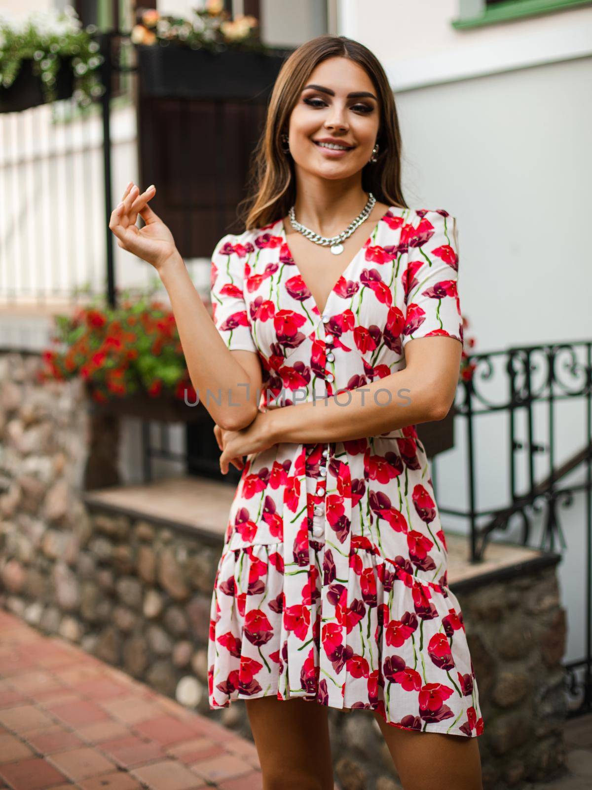 young cheerful woman with long dark hair wearing white dress with red flowers smiling to the camera by StudioLucky