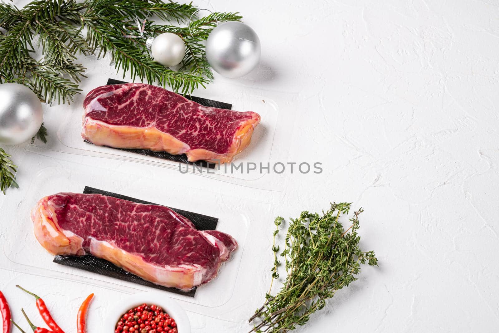Raw steak with Christmas tree decorations set, on white stone table background, with copy space for text