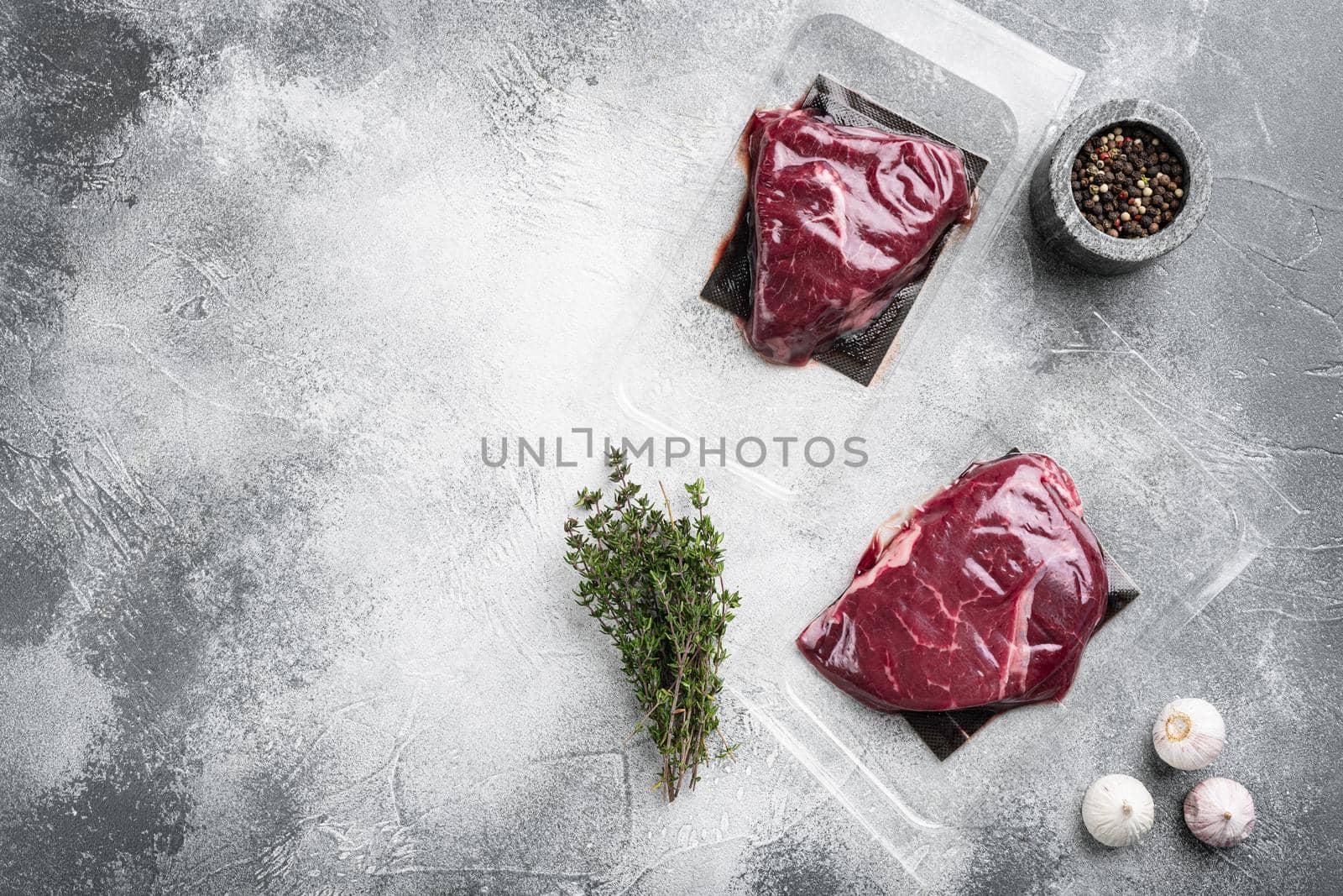 Beef steak vacuum sealed set, on gray stone table background, top view flat lay, with copy space for text