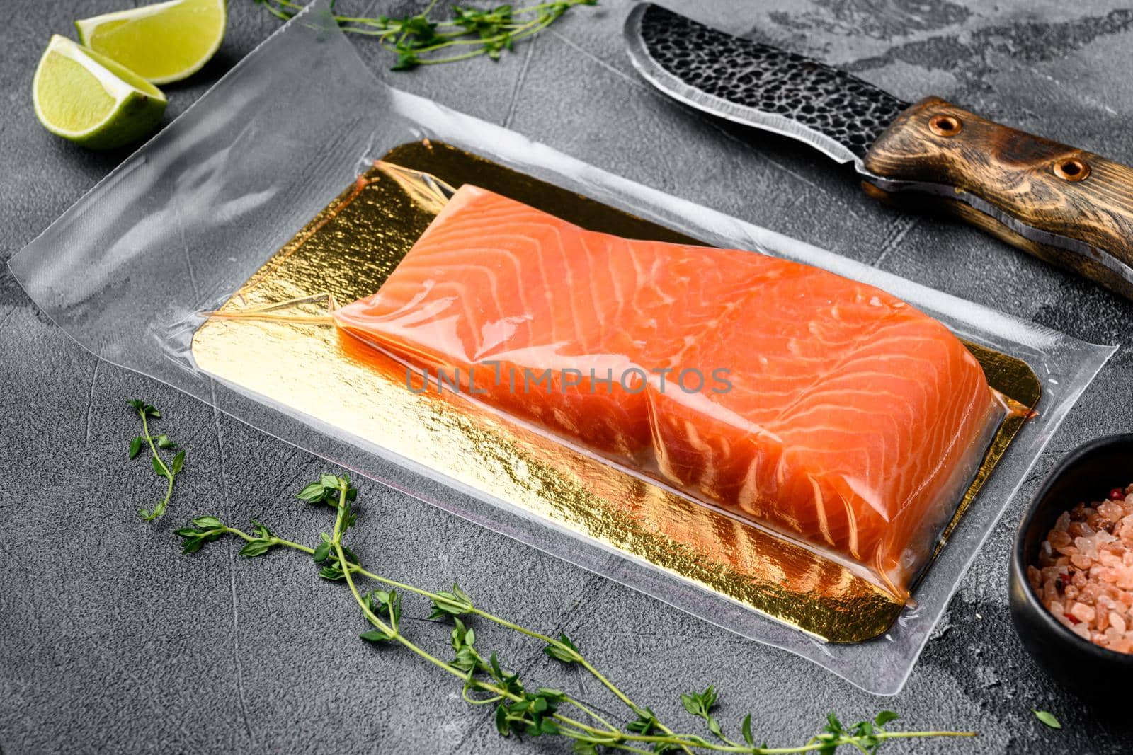 Fresh raw salmon fish steak in vacuum pack set, with herbs, on gray stone table background, with copy space for text
