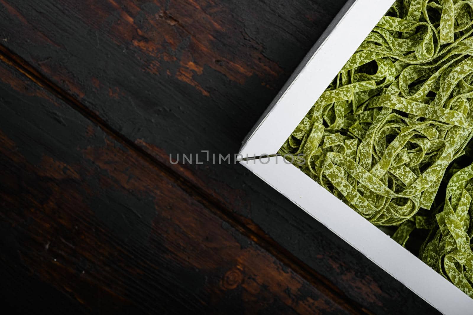 Colorful raw italian tagliatelle pasta in box set, on old dark wooden table background, top view flat lay, with copy space for text