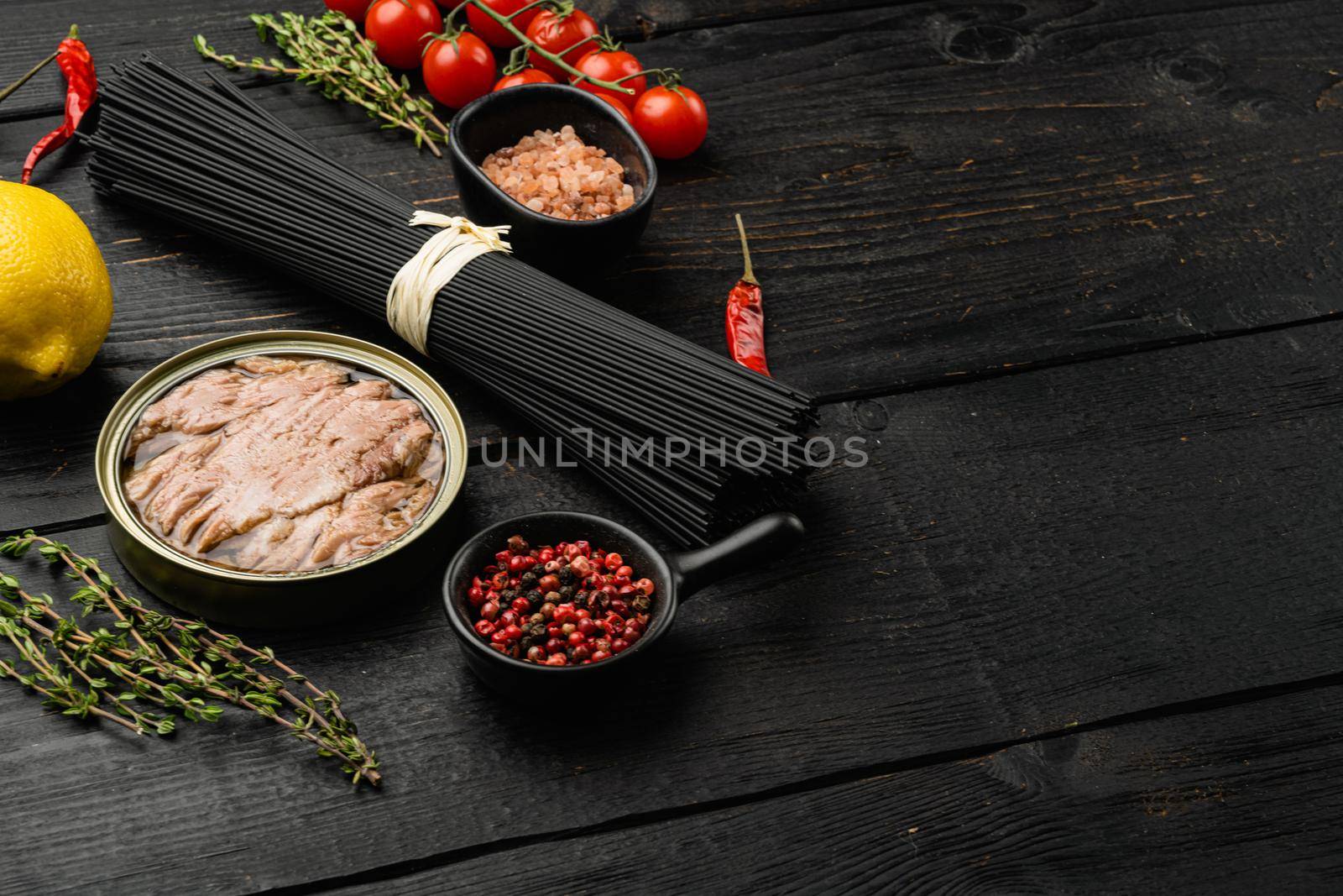 Ingredients uncooked pasta with tuna and tomatoes set, on black wooden table background, with copy space for text