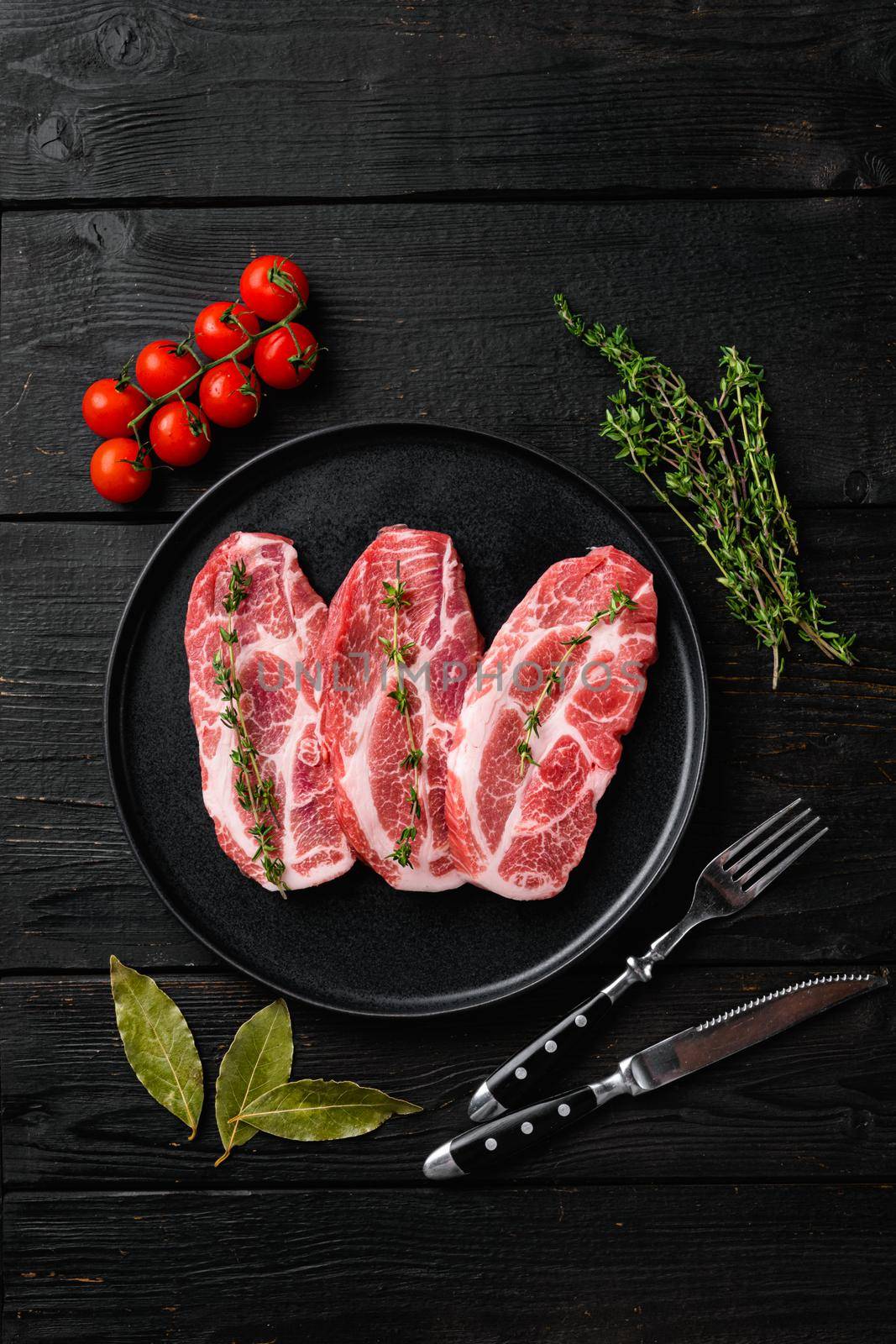 Raw pork neck chop meat with herb leaves and spice, on black wooden table background, top view flat lay by Ilianesolenyi