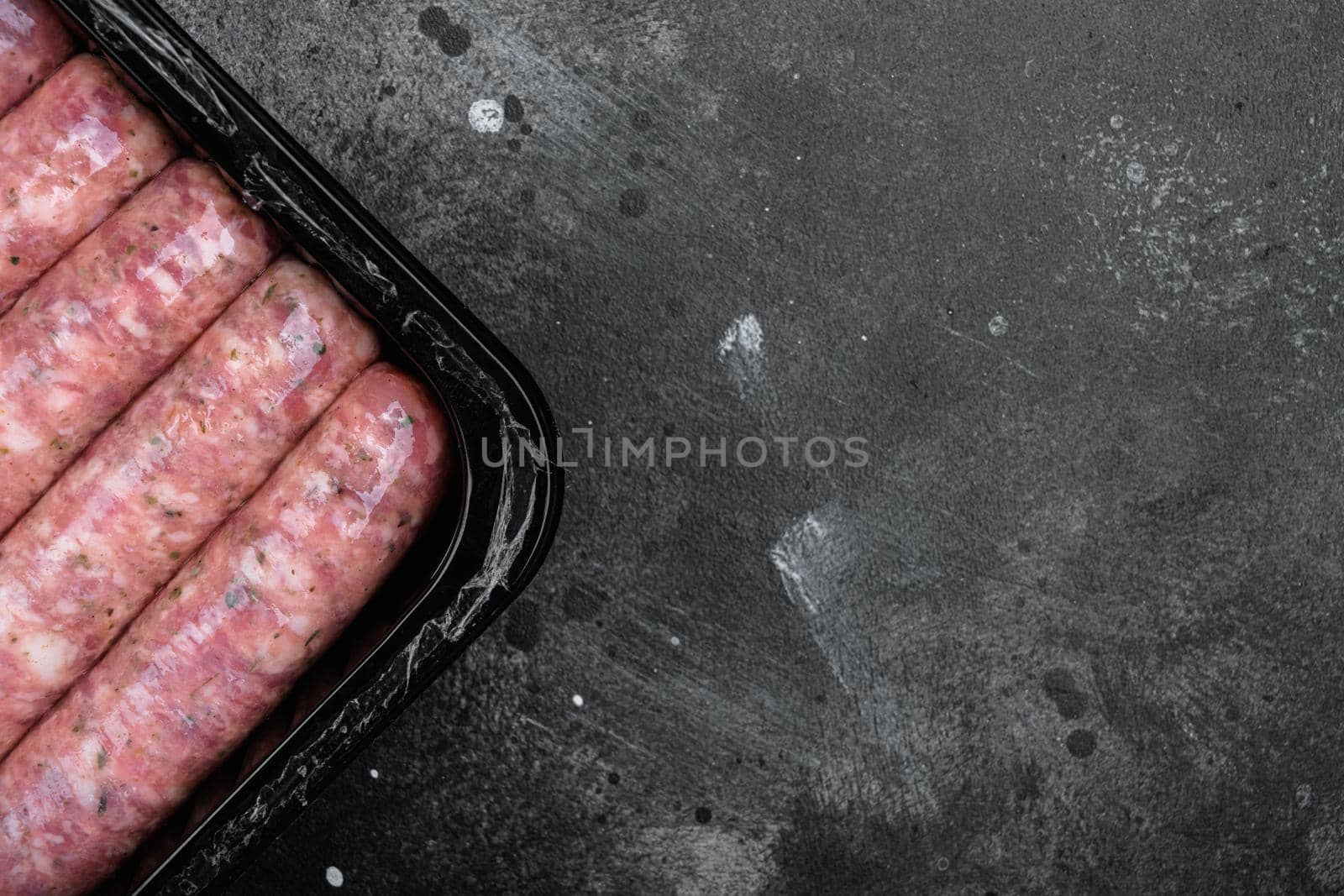 Uncooked meat sausages in plastic pack set, on black dark stone table background, top view flat lay, with copy space for text