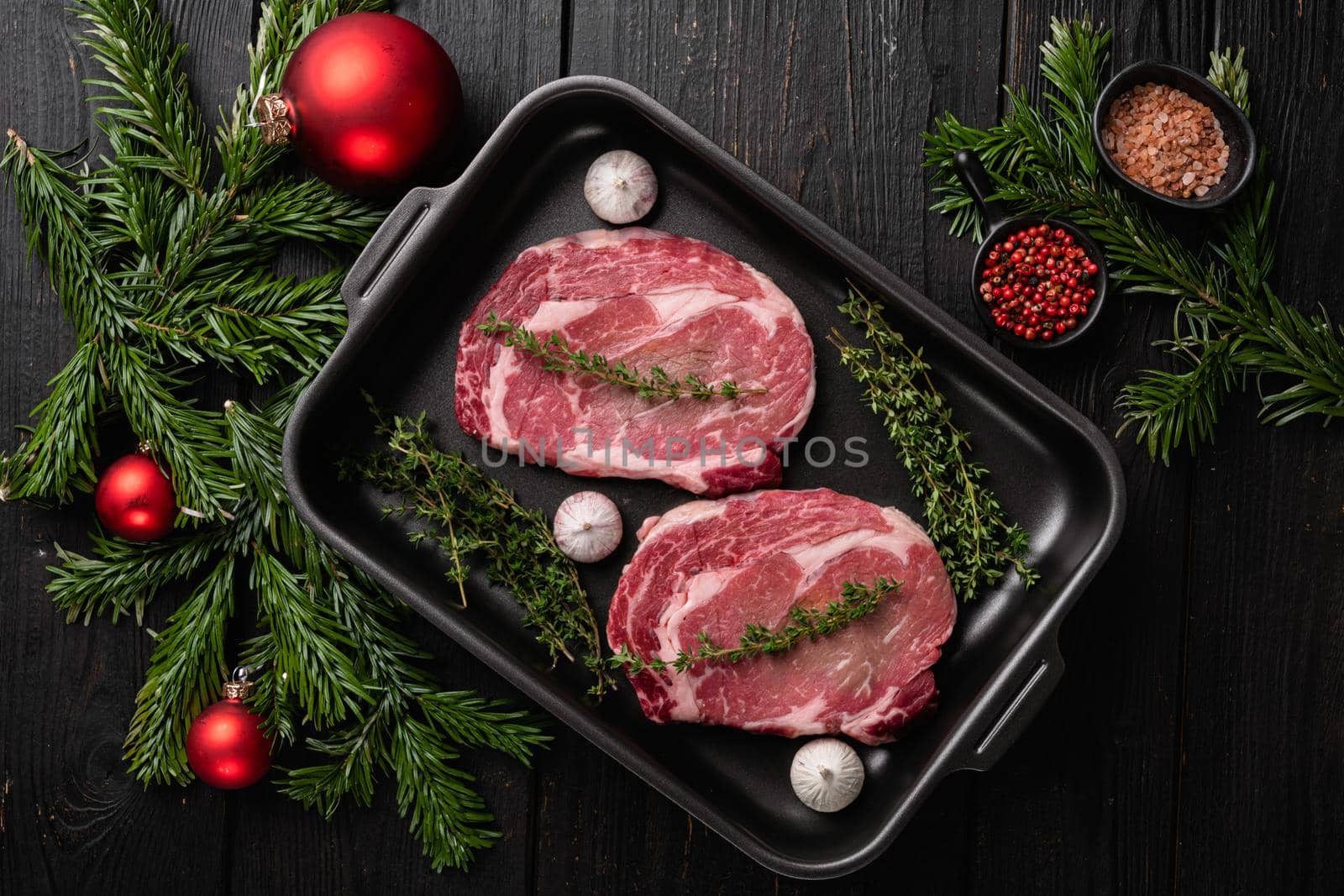 Raw rib eye beef steak with pepper and herbs to the Christmas and New Year, on black wooden table background, top view flat lay by Ilianesolenyi