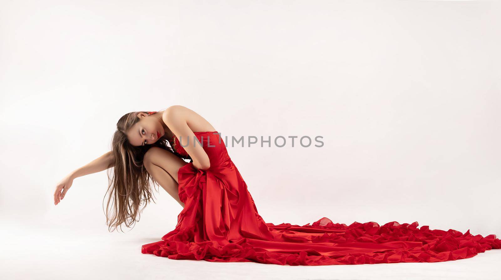 the beautiful slender girl in a red long dress on a white background on the floor