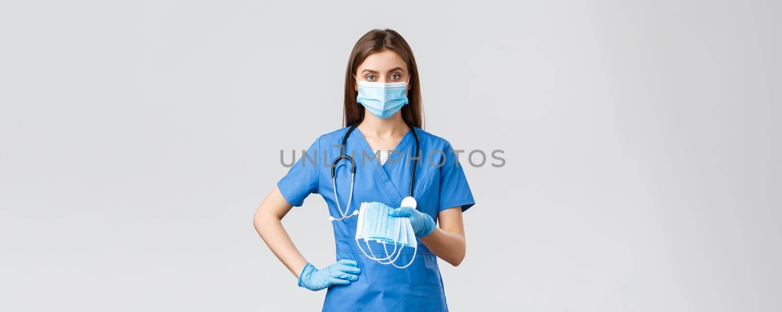 Covid-19, preventing virus, health, healthcare workers and quarantine concept. Young doctor or female nurse in blue scrubs and protective equipment against coronavirus infection, give medical masks by Benzoix