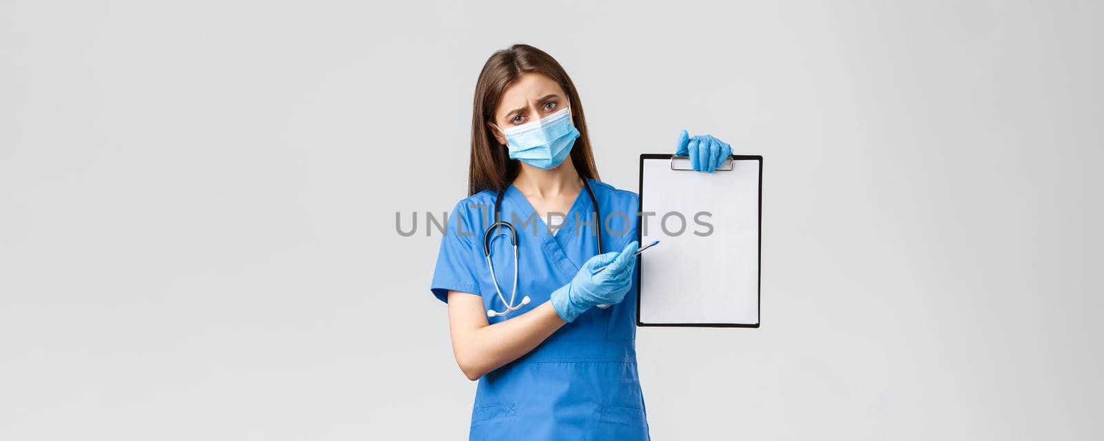 Covid-19, preventing virus, healthcare workers and quarantine concept. Tired concerned female nurse or doctor in blue scrubs, medical mask, explain importance use masks and gloves during coronavirus.