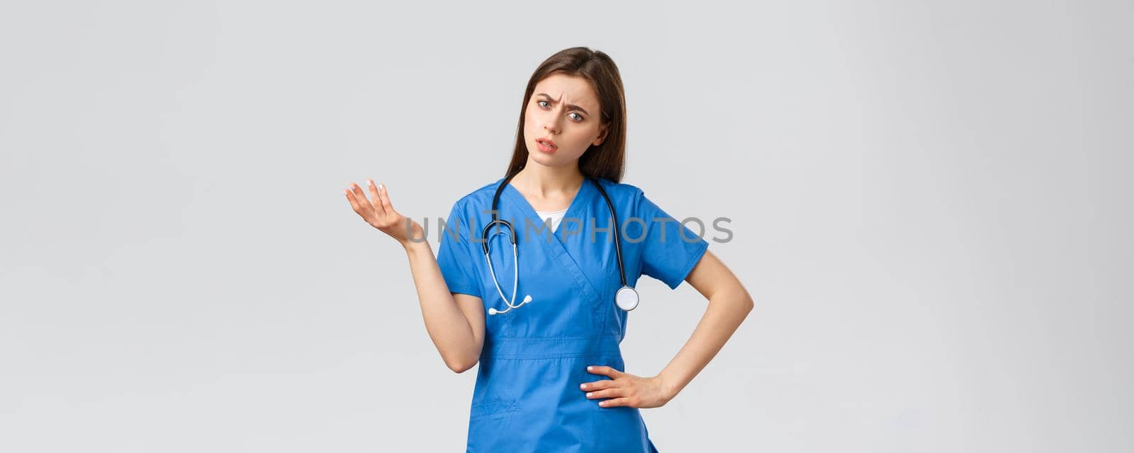 Healthcare workers, prevent virus, insurance and medicine concept. Confused and puzzled female nurse, doctor in scrubs with stethoscope, shrugging and lift hand, stare indecisive, cant understand.