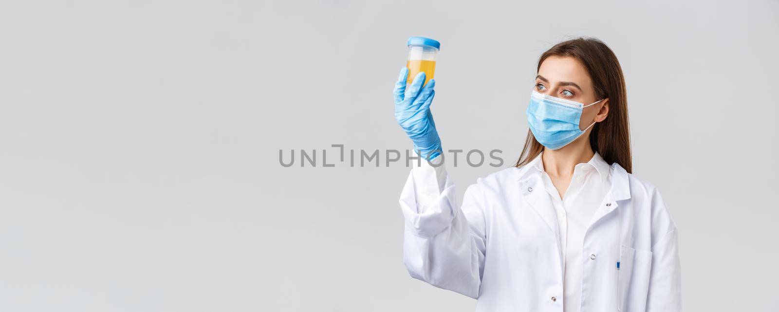 Covid-19, medical research, diagnosis, healthcare workers concept. Professional doctor in clinic lab, scrubs and medical mask, looking at urine sample, patient test on coronavirus infection.