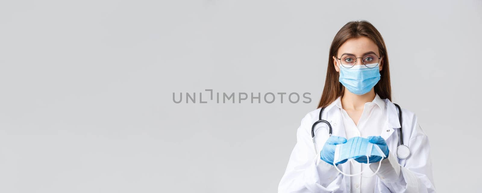 Covid-19, preventing virus, clinic, healthcare workers and quarantine concept. Young doctor in medical mask and gloves, white scrubs, giving face mask protection to patients, look serious.