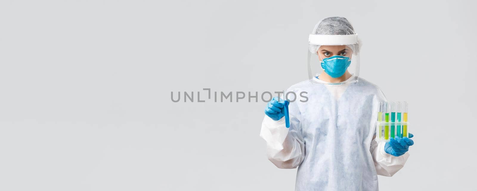 Covid-19, medical research, diagnosis, healthcare workers and quarantine concept. Doctor in personal protective equipment hold test-tubes with coronavirus vaccines, working in clinic laboratory.