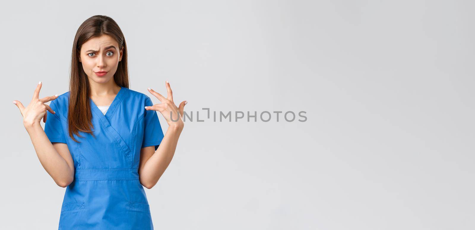 Healthcare workers, prevent virus, insurance and medicine concept. Funny displeased female nurse in blue scrubs grimacing, freak out over something, mimicking and staring camera shocked.