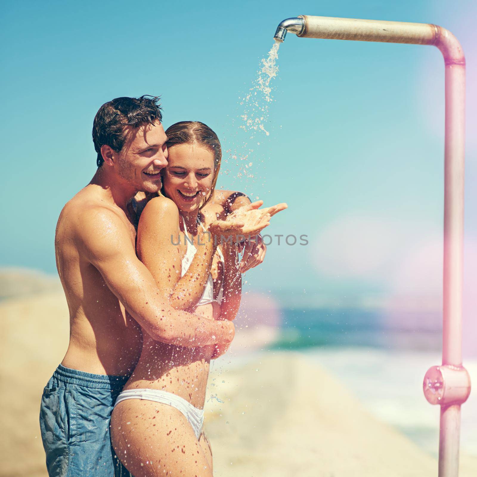 Youre supposed to be washing me. Cropped shot of an affectionate young couple showering on the beach. by YuriArcurs