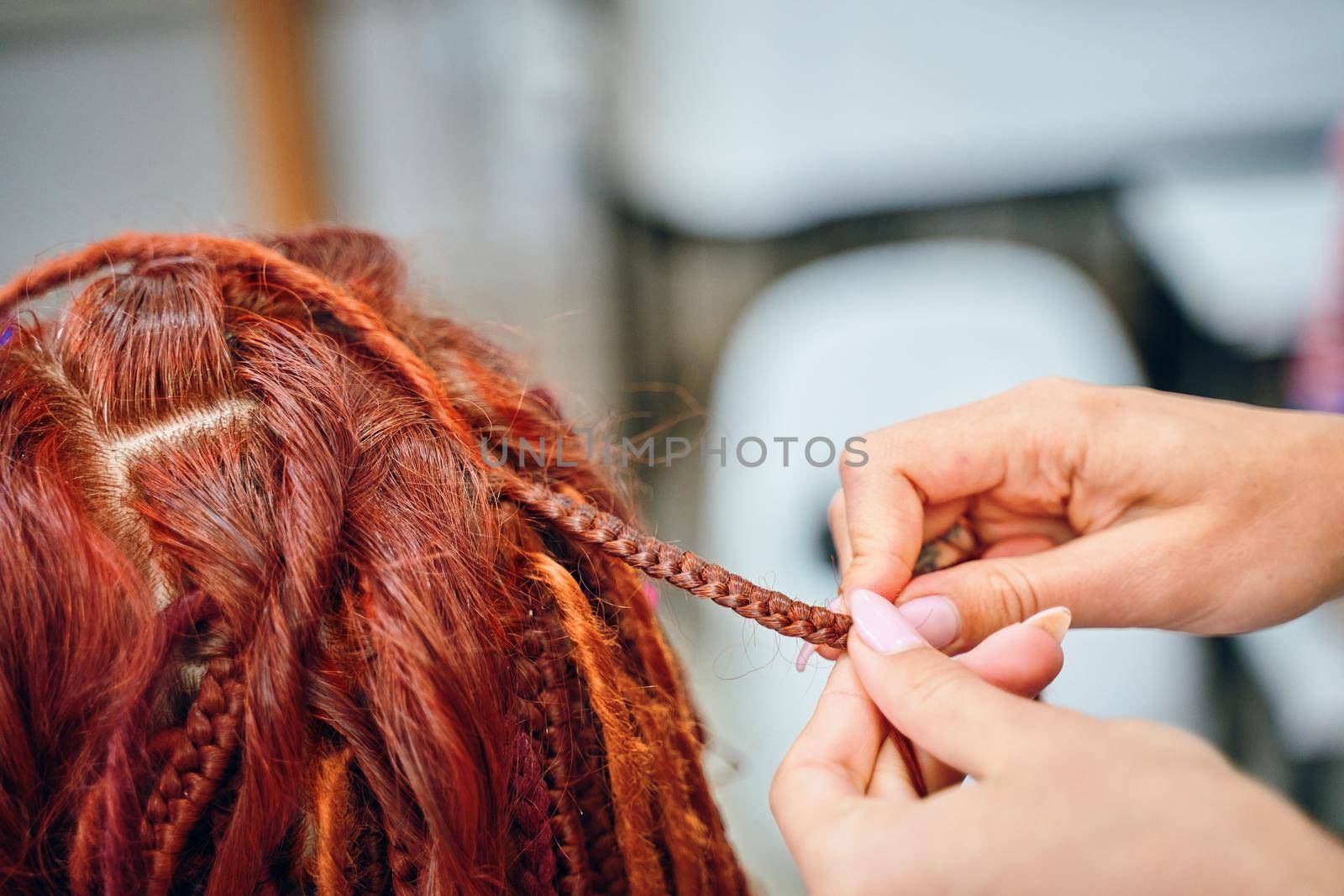 Braiding process plait with colored kanekalon. Beauty salon services. Girl hairdresser weaves woman ginger dreadlocks. Bright pigtails on head. Hippie style hairstyle.