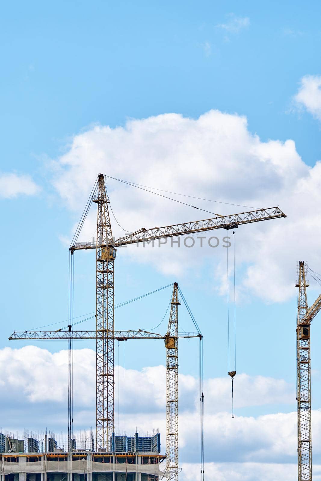 Construction site background with copy space. Industrial building cranes on background of cloudy sky. Hoisting cranes for creating multi-storey buildings of new city districts.