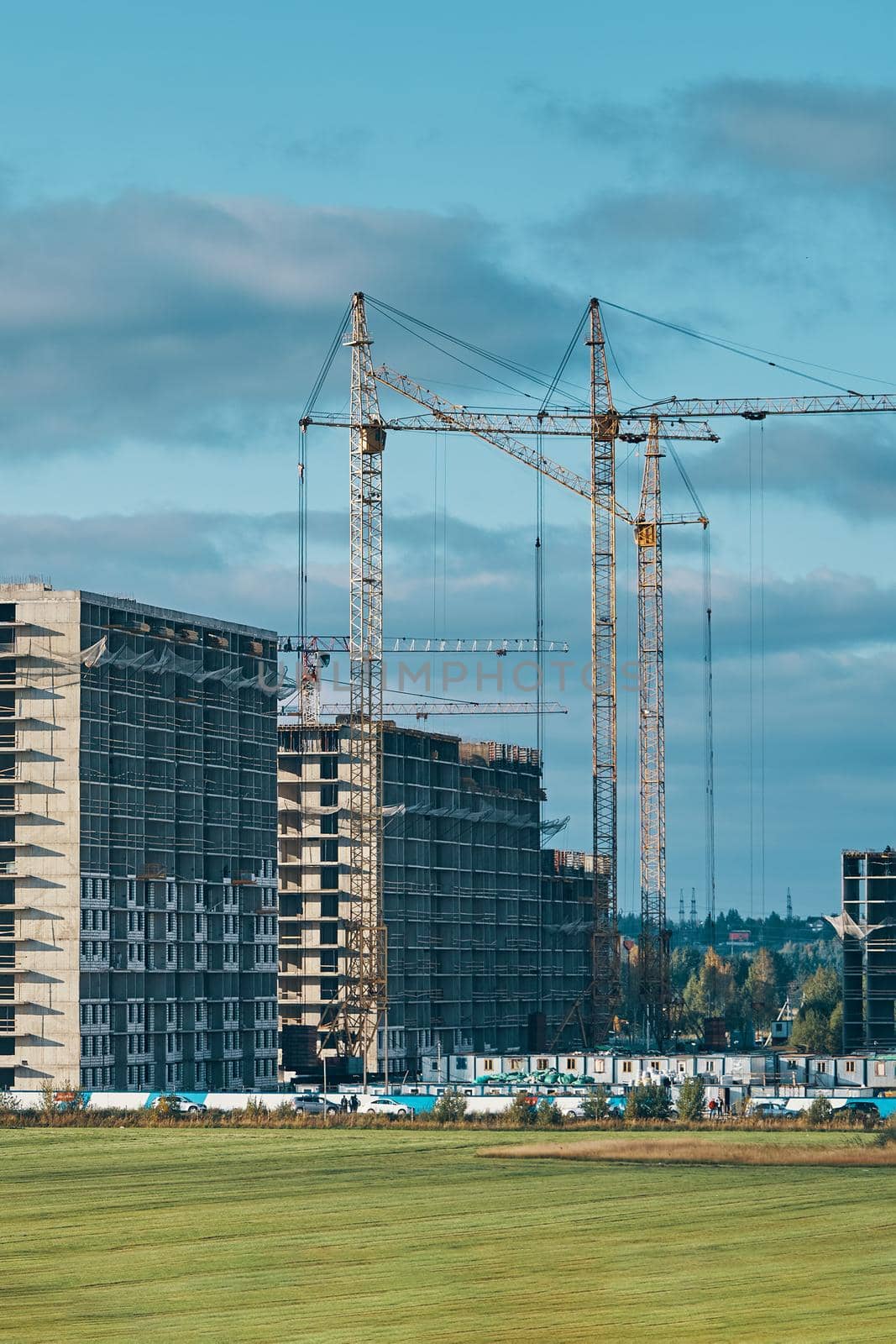 Building site background. Industrial construction cranes on background of clouds sky. Hoisting cranes, multi-storey buildings of new city districts and large green field. Project of urban area.