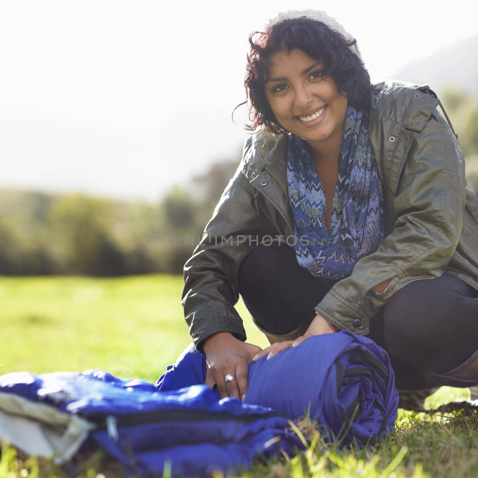 Attractive young woman unrolling a sleeping bag on the grass.