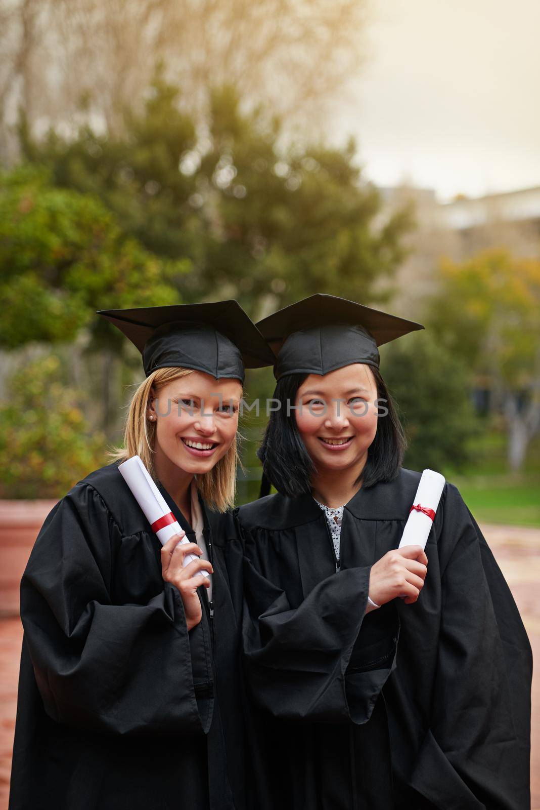 Were ready for our next adventure. Shot of two college graduates holding their diplomas. by YuriArcurs