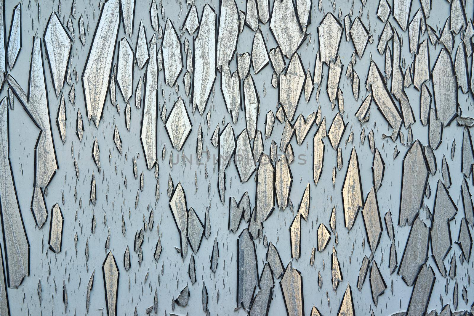 Grey paint cracks and peels off of a reflective metallic surface