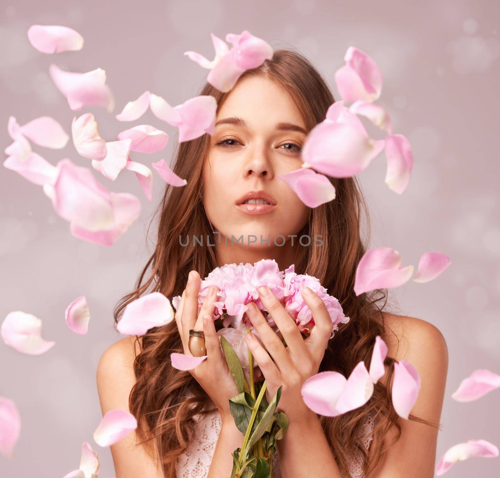 Gorgeous young woman surrounded by rose petals on a pink background.