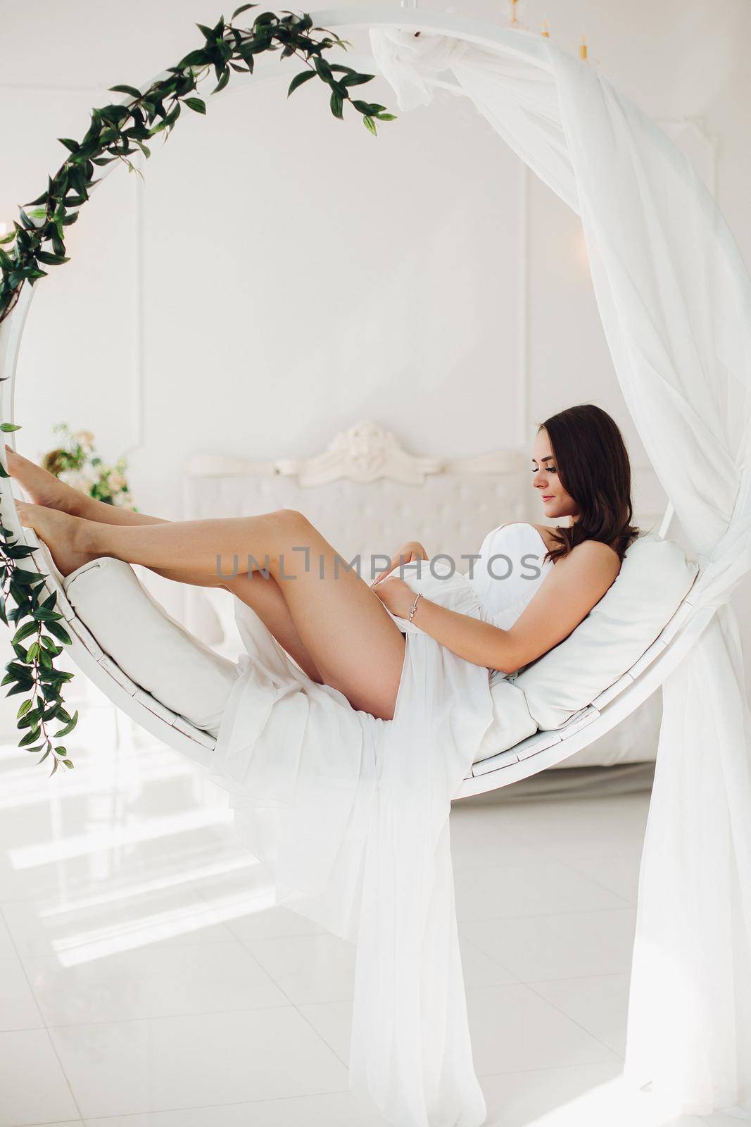 Gorgeous pregnant woman in white gown on designed chair. by StudioLucky