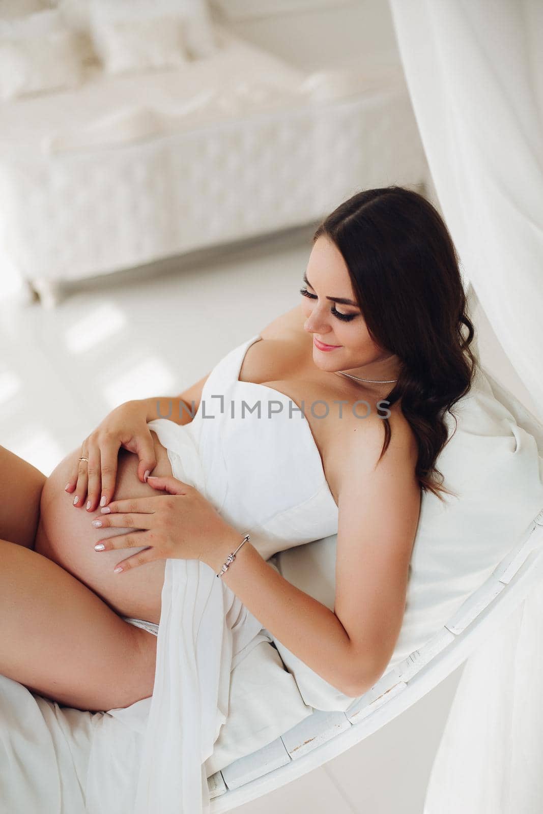 Pregnant woman in white dress lying on bed and resting by StudioLucky