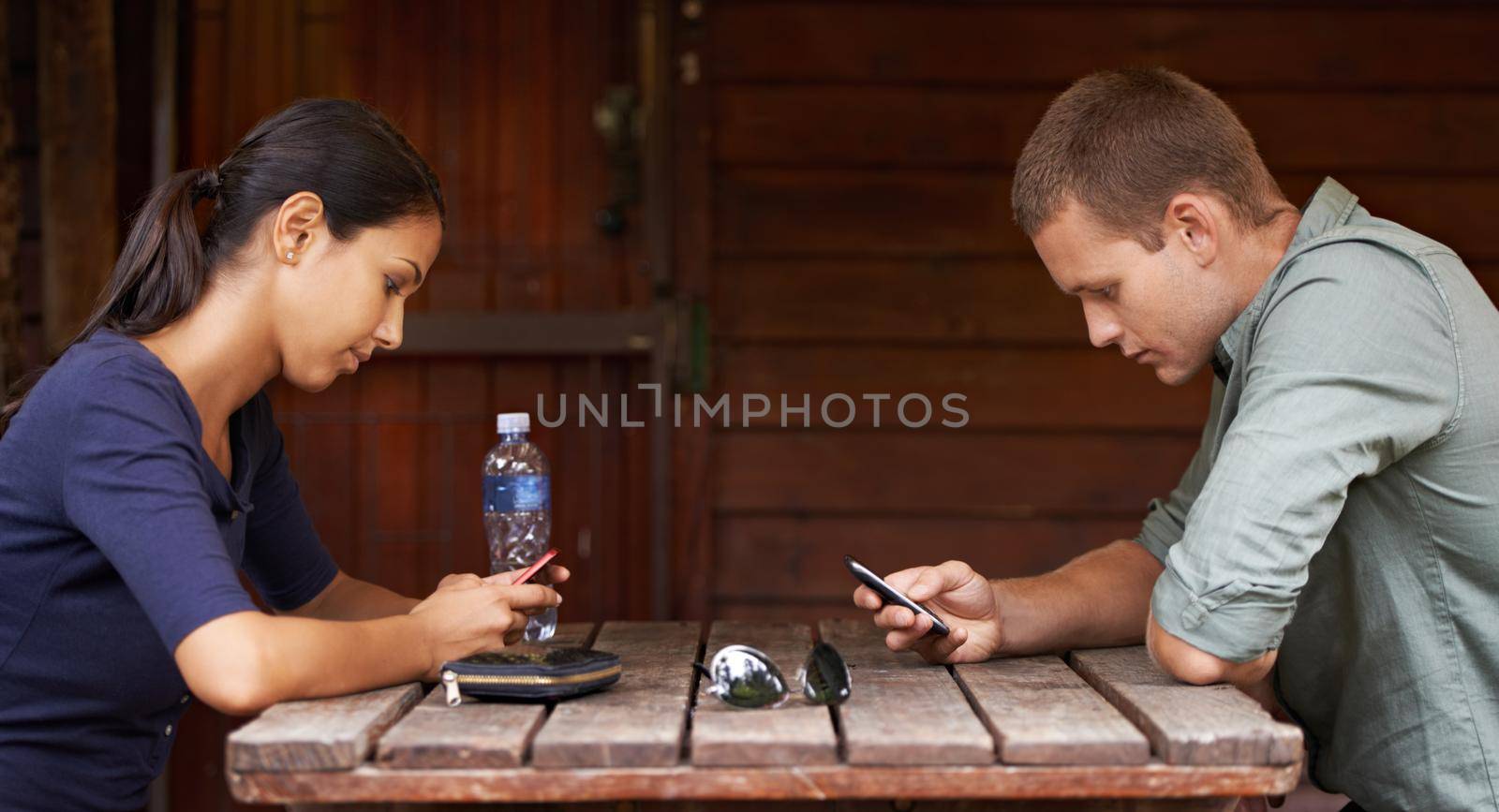 Two young adults being distracted by technology while out on a coffee date.