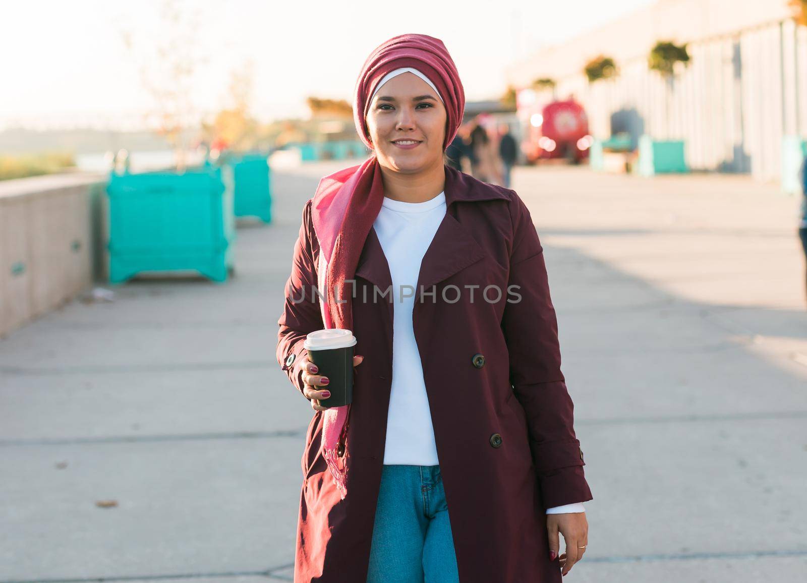 Young Arabic muslim woman in hijab walking at street seafront and drinking coffee take away by Satura86