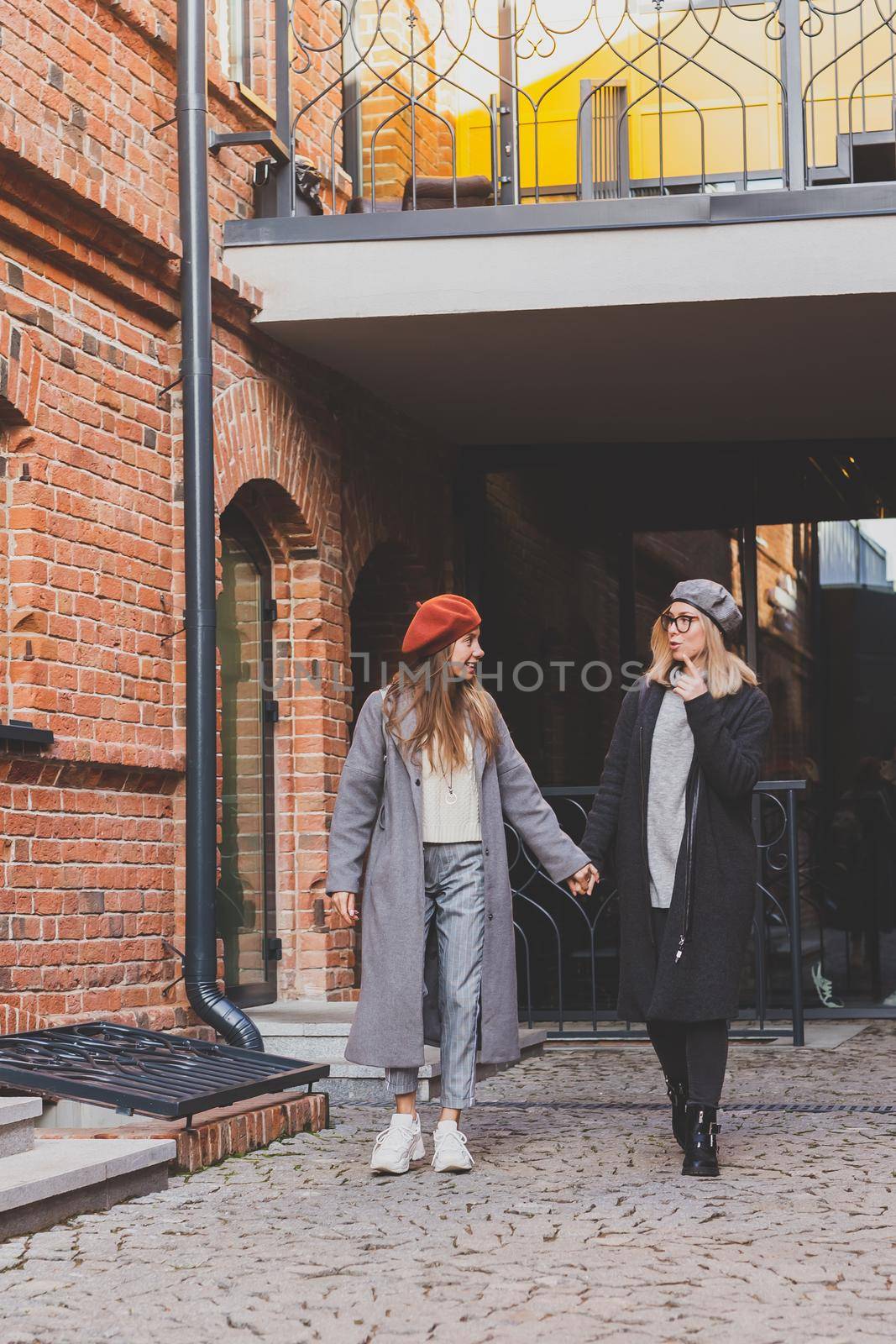 Two girls walking on street together and holding their hands. They are wearing spring or autumn clothes and they happy. Friendship and relationship concept