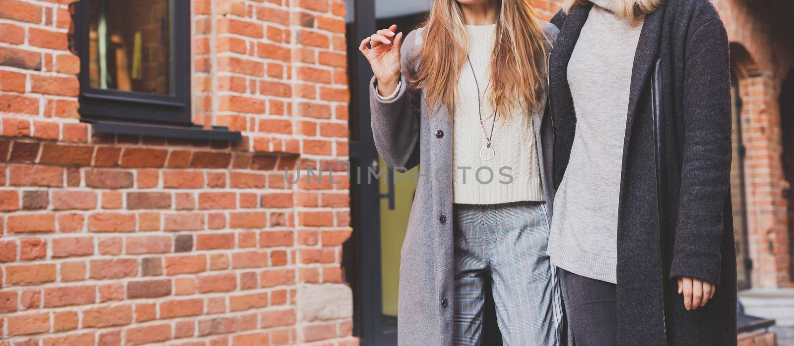 Two girls walking on street together and holding their hands. They are wearing spring or autumn clothes and they happy. Friendship and relationship concept