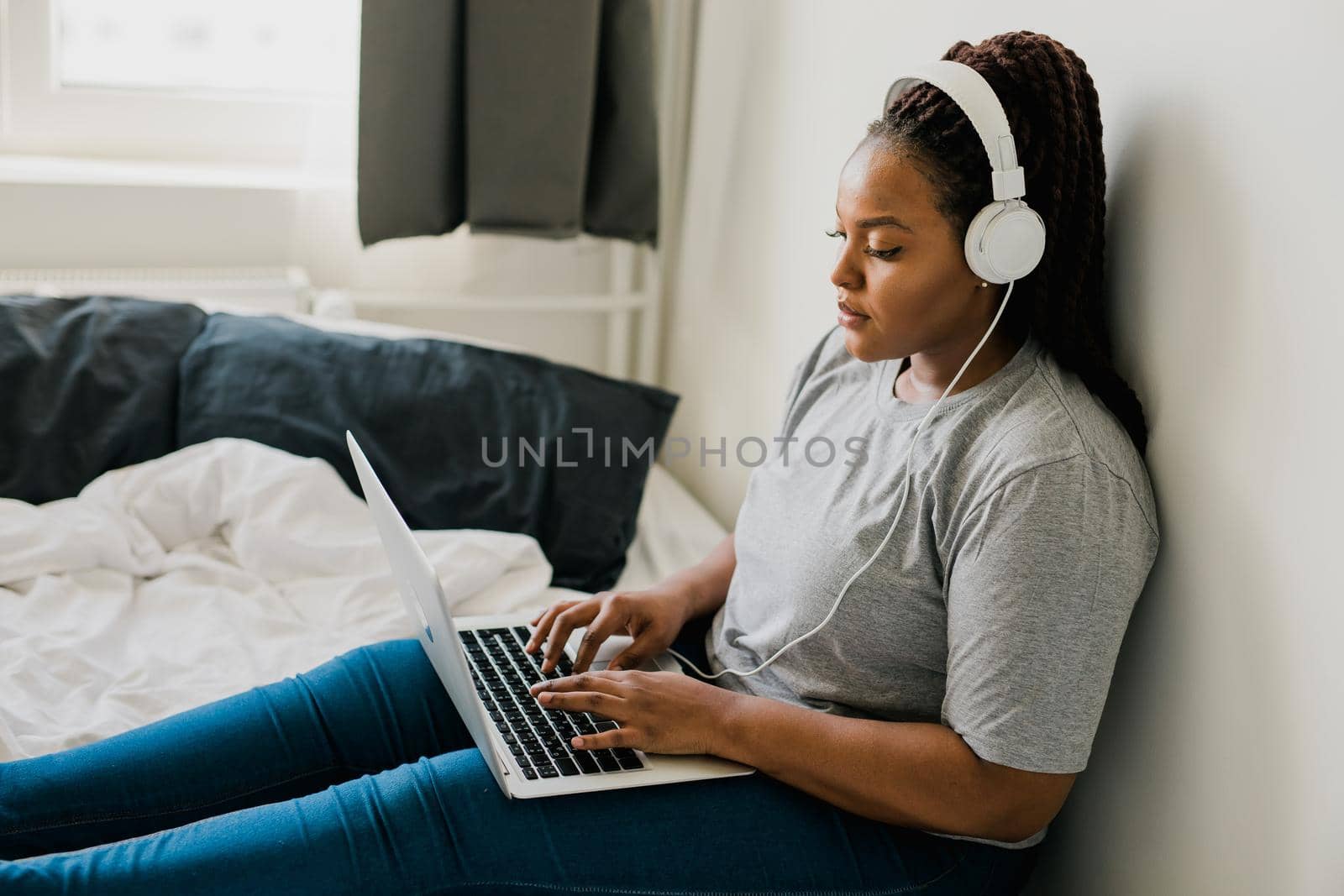 African american young woman using laptop with headphones on bed - technologies and communication and social network concept by Satura86