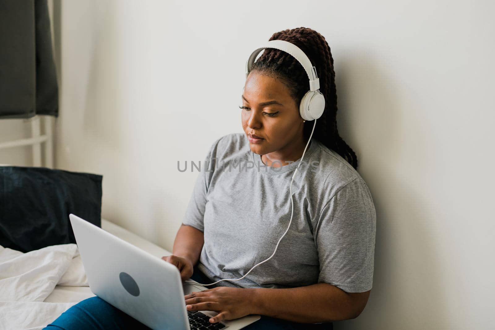 African american young woman using laptop with headphones on bed - technologies and communication and social network concept by Satura86
