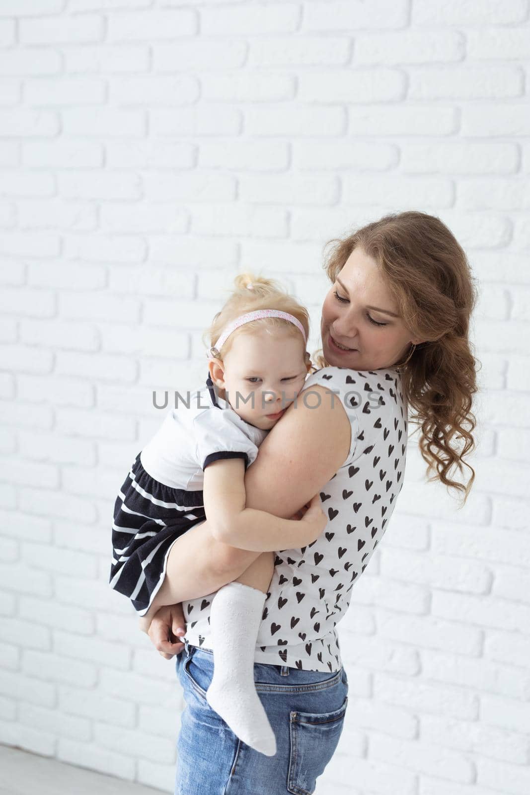 Mother holds her child with hearing aids and cochlear implants on white brick wall . Deaf and health concept by Satura86