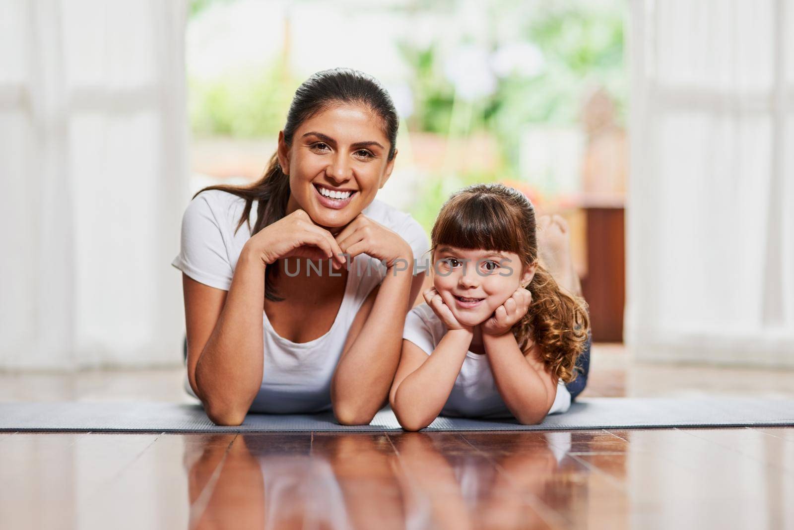 Portrait of a cheerful mother and daughter lying on the ground while resting their faces in their hands.