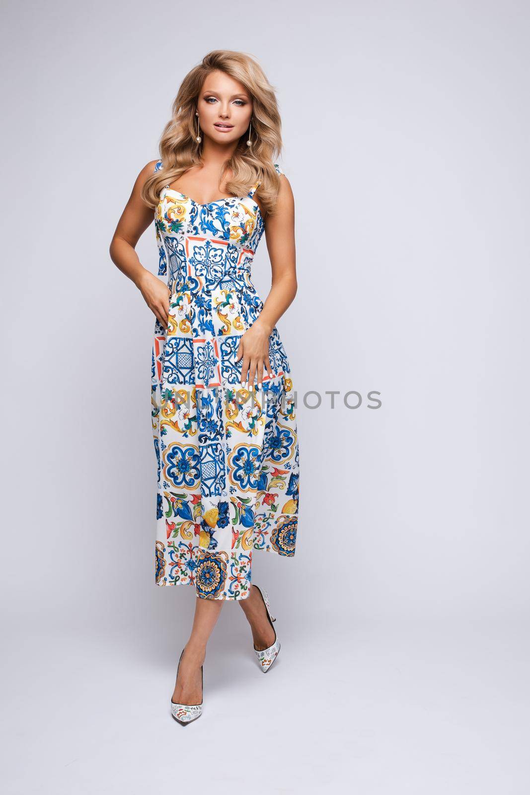 Front view of slim blonde standing on black isolated background and posing. Attractive young woman in long dress looking at camera and smiling in studio. Concept of elegance and glamour.