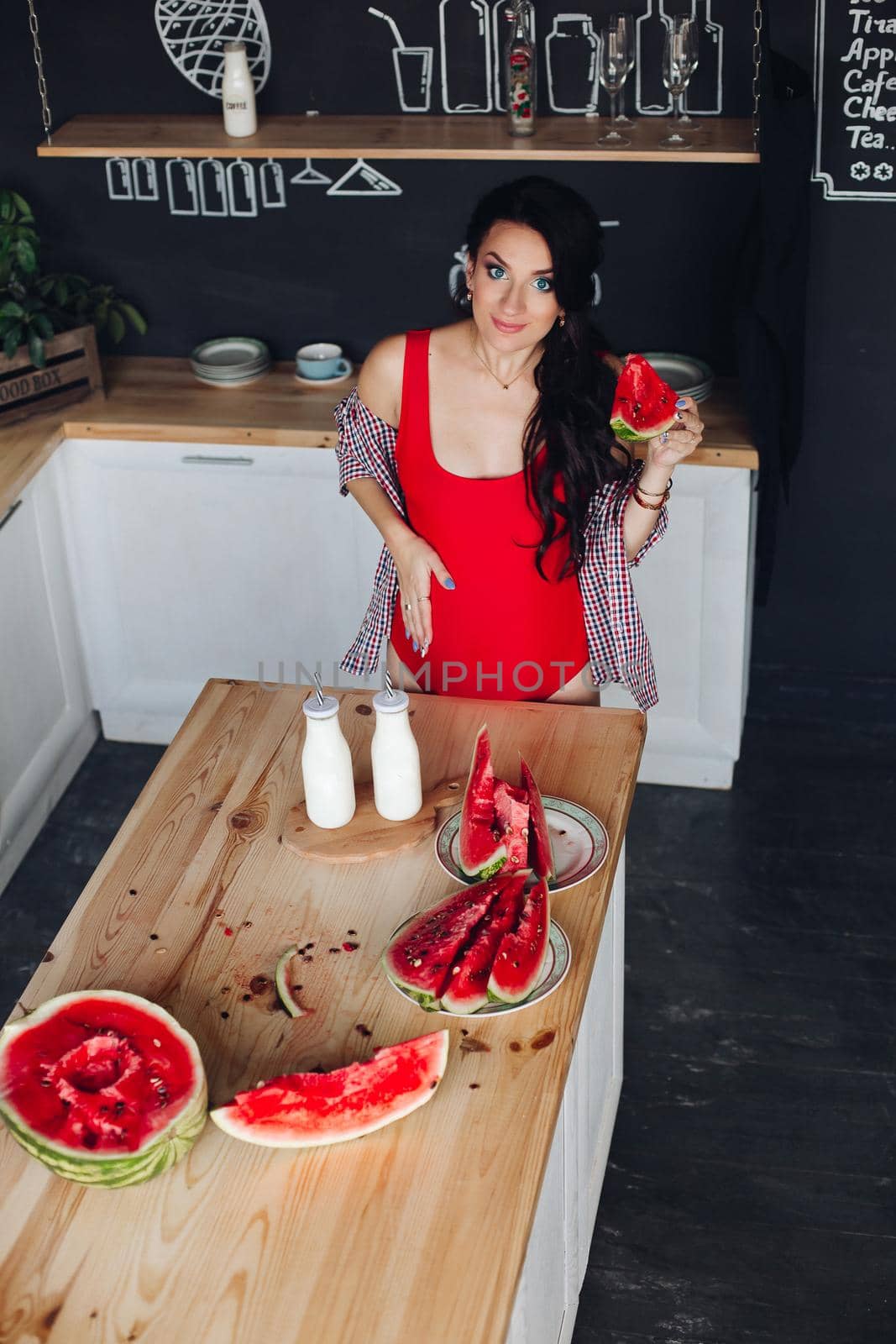 Adorable pregnant woman standing at kitchen and touching big belly with hands. Attractive brunette expecting little child and enjoying motherhood. Concept of love and pregnancy.