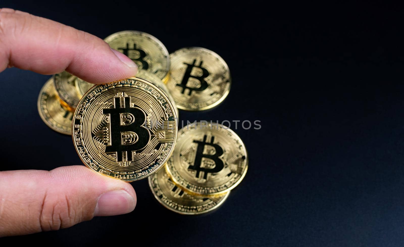 Human fingers holding bitcoins on a black background by Unimages2527