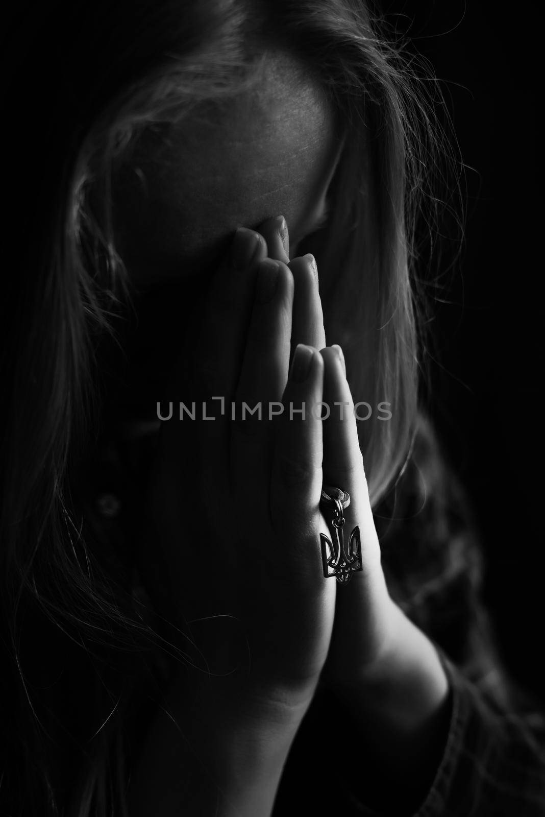 Ukrainian blonde woman prays for Ukraine during the war with the state emblem Trident in her hands. Russia attacked Ukraine on February 24, 2022. Black and white vertical photo