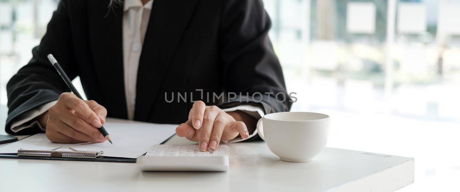 Crop shot of accountant woman hand press on calculator and writing a note for make financial report or company's profit annual at desk, bookkeeper job by nateemee